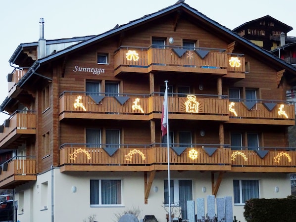 Ein mehrstöckiges Holzhaus mit Balkonen, einem Schild mit der Aufschrift 'Sunnegga' und einer Fahnenstange mit einer Flagge.