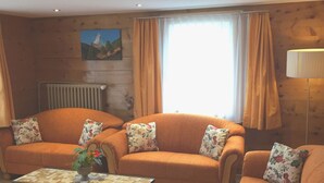 Un salon avec deux canapés orange, une petite table sur laquelle est pos é un vase, un radiateur et un tableau accroché au mur.
