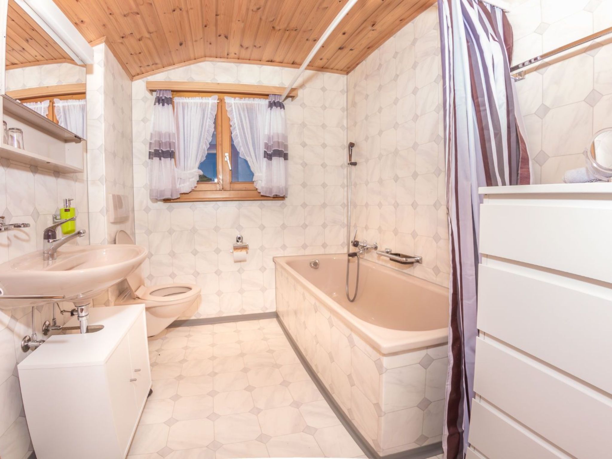Een badkamer met houten plafond, een badkuip, toilet en wastafel.