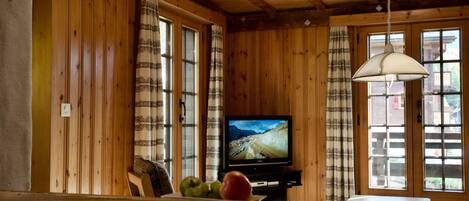 Un interior de madera con un televisor sobre un mueble bajo, un banco y una mesa.