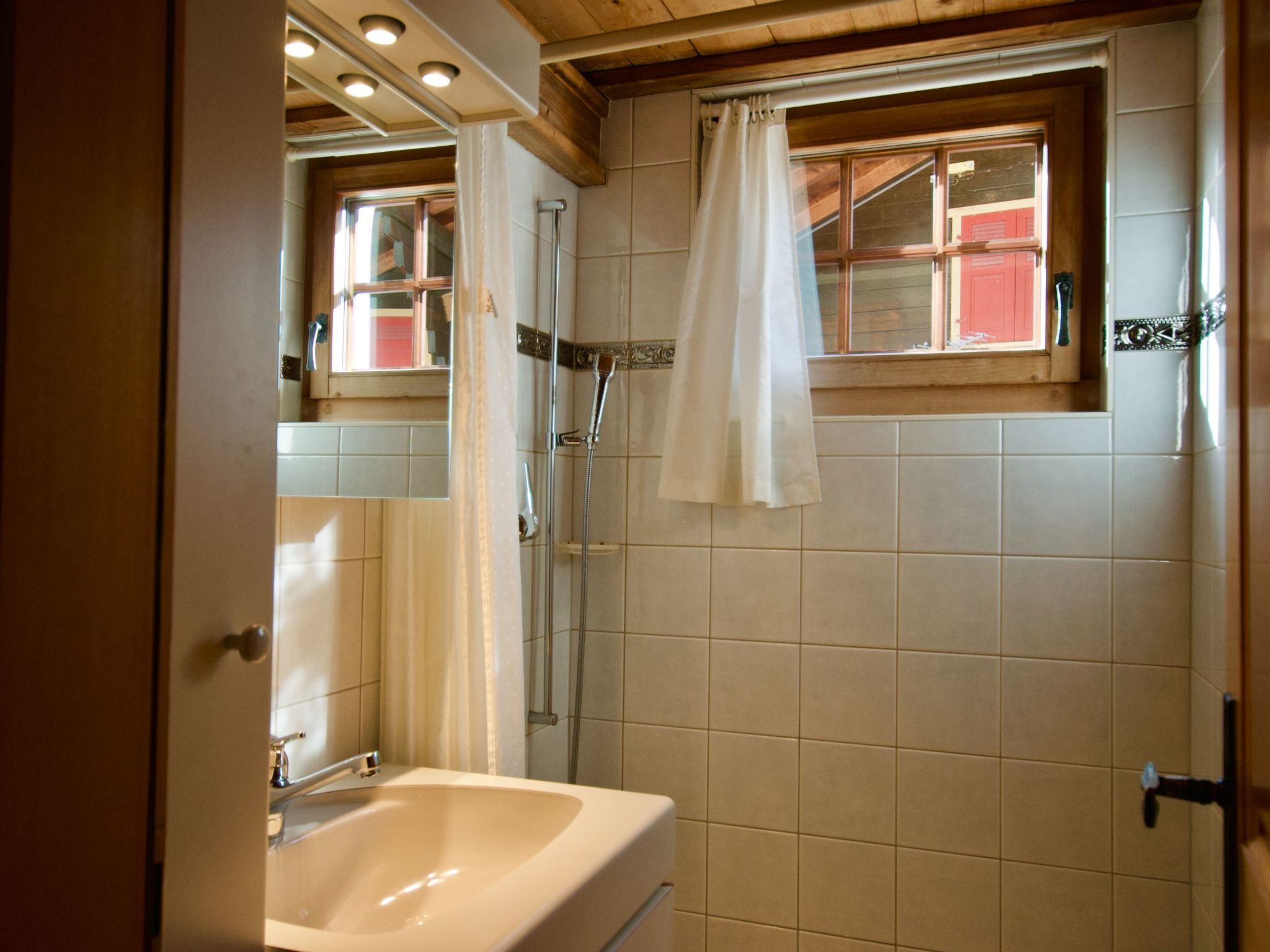 A bathroom with a shower, a sink, and a window with a curtain.