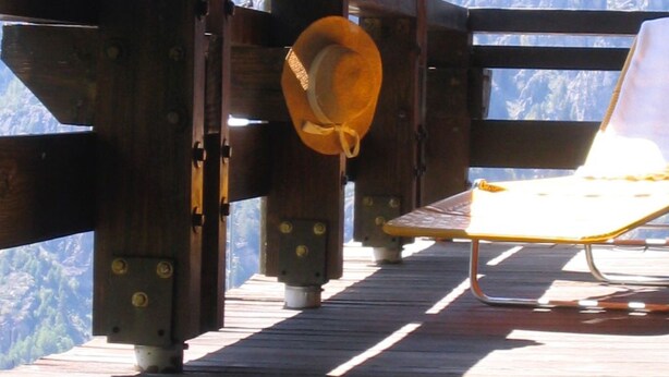 Una terraza de madera con un banco y un perchero, con vistas a un paisaje montañoso.