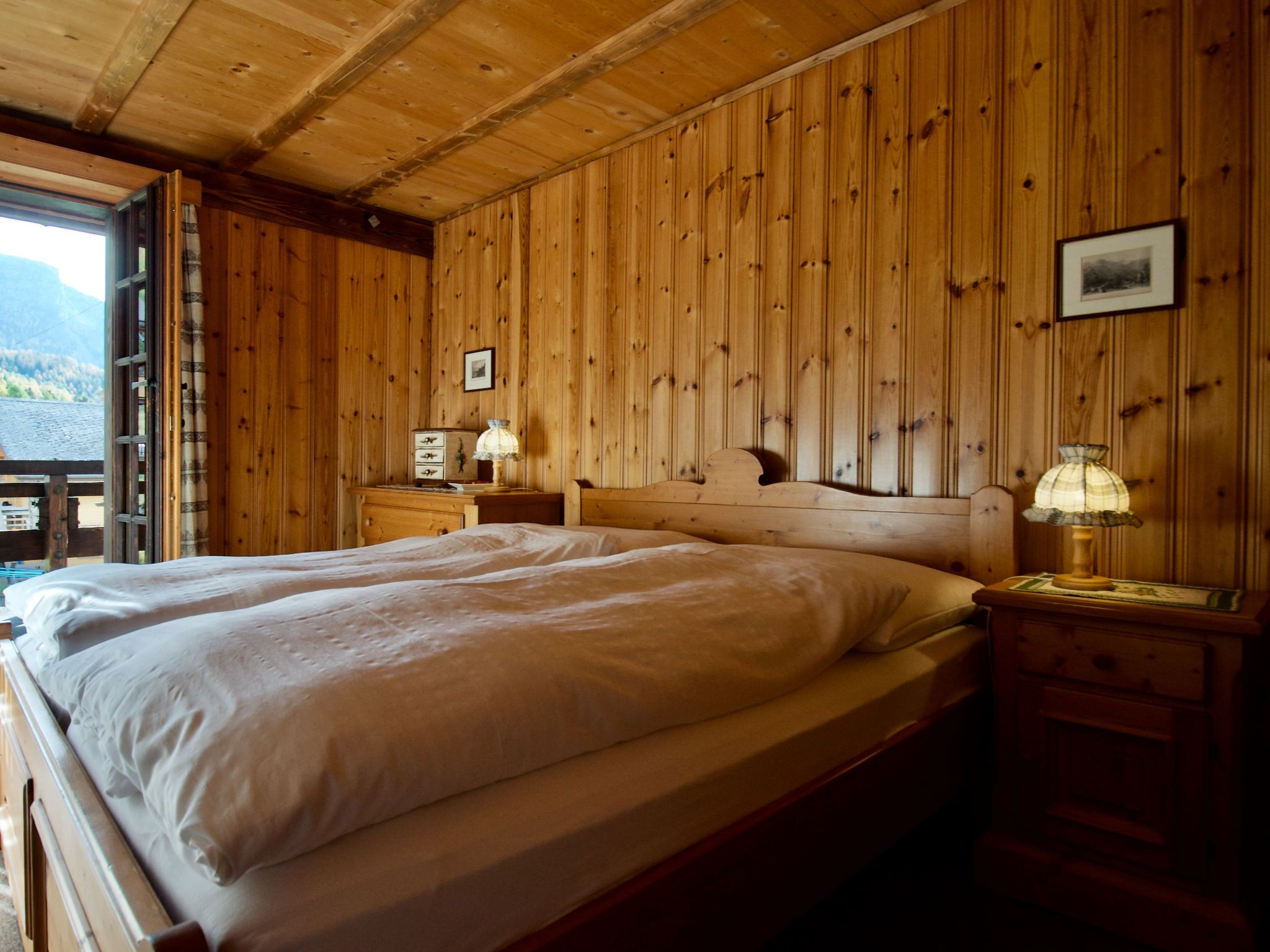 Um quarto de madeira com uma cama, duas mesas de cabeceira e uma janela.