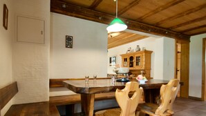 Una mesa de comedor de madera con sillas, una lámpara colgante y una cocina al fondo.