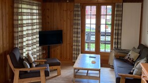 Un interior de madera con televisor, sofá, sillón y mesa.