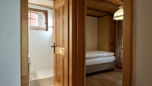 Una habitación con puerta de madera, ventana, cama y una lámpara en el techo.