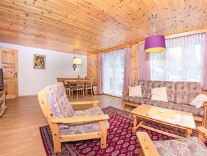 Ein Wohnzimmer mit Holzboden, ausgestattet mit einer Couch, Sesseln, einem Couchtisch und einem Essbereich mit Stühlen.
