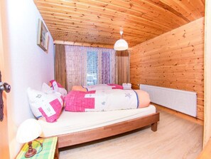 A cozy wooden room with a bed, a window with curtains, and a radiator. - Ferienwohnungen Fleurs des Alpes, (Grächen), by Interhome (Grächen)