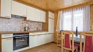 A kitchen with wooden cabinets, a stove, and a dining area with chairs.