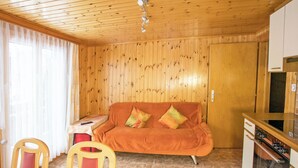 A wooden-paneled room with a sofa, a table, chairs, and a kitchen area.