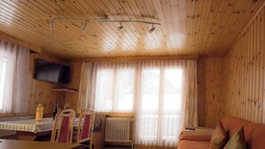 A wooden-paneled room with a sofa, a table, chairs, a radiator, and a TV mounted on the wall.