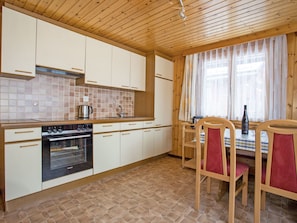 A kitchen with white cabinets, a Siemens oven, a tiled backsplash, and a dining area with a table and chairs. - Ferienwohnungen Bergtreu, (Grächen), by Interhome (Grächen)