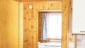 A wooden room with a bed, a window with curtains, and a kitchenette.