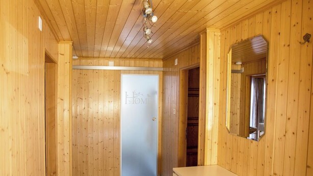 A room with wooden walls and ceiling, a white desk, a bench, and a door labeled 'HOME'.