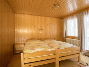 A wooden-paneled room with a bed, a nightstand, a window with curtains, and a radiator. - Ferienwohnungen Bergtreu, (Grächen), by Interhome (Grächen)