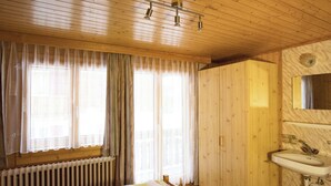 A wooden-paneled room with a bed, a window with curtains, a radiator, and a bathroom with a sink and mirror. - Bergtreu, (Grächen), by Interhome (Grächen)