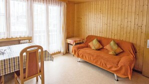A cozy room with a wooden ceiling, a sofa with cushions, a table with a checkered tablecloth, and a window with sheer curtains. - Bergtreu, (Grächen), by Interhome (Grächen)