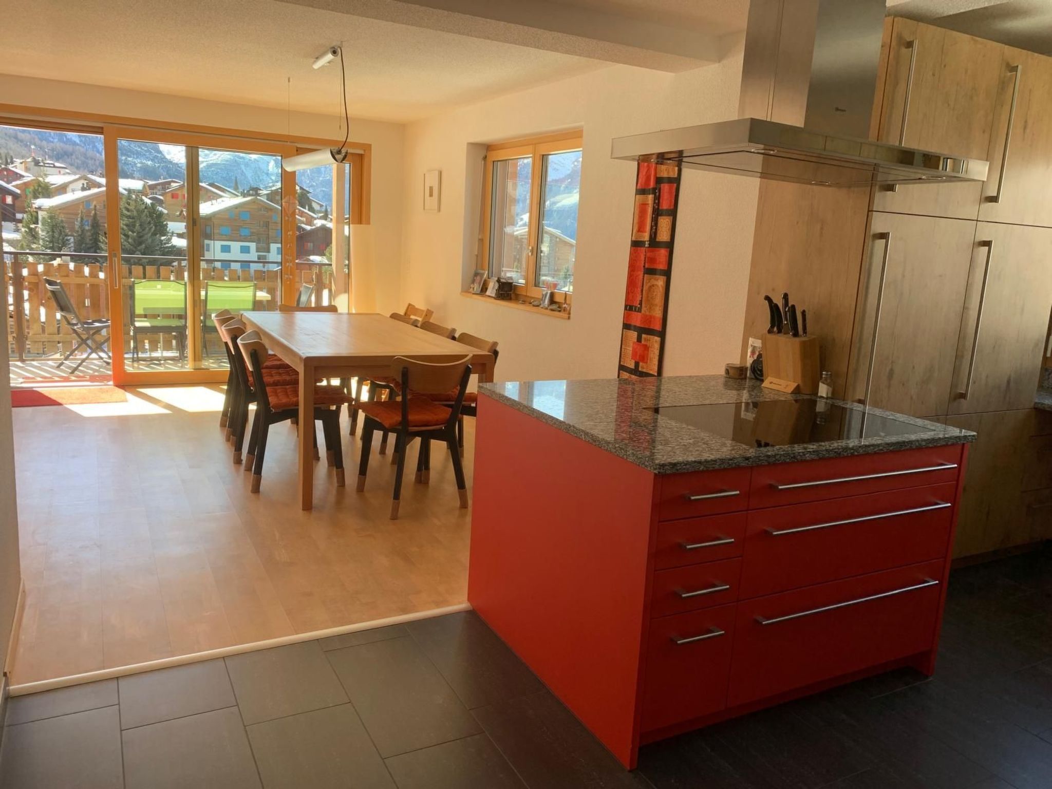 A modern kitchen with a red island, wooden cabinets, and a dining area with a table and chairs.