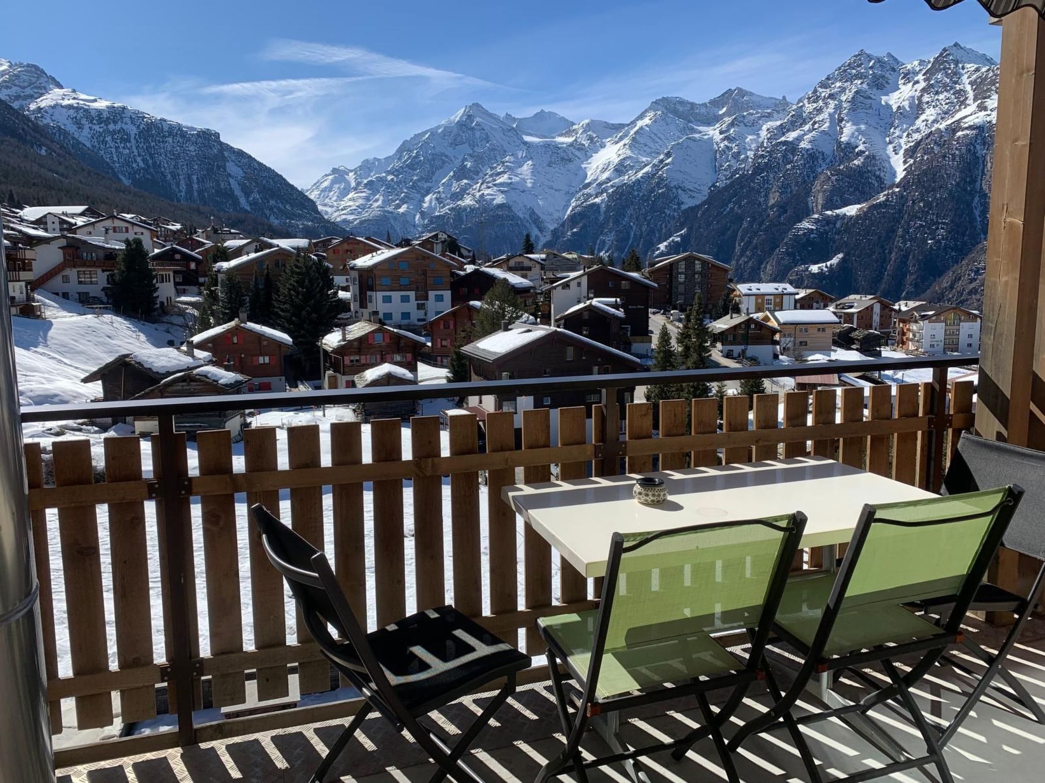 A balcony with a table and chairs overlooking a snow-covered mountain village.