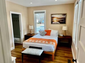 A bedroom with a bed, two bedside tables, a window, and a door. - The Little Retreat Unit A - Walk to Shops & Beach (Cape Charles)