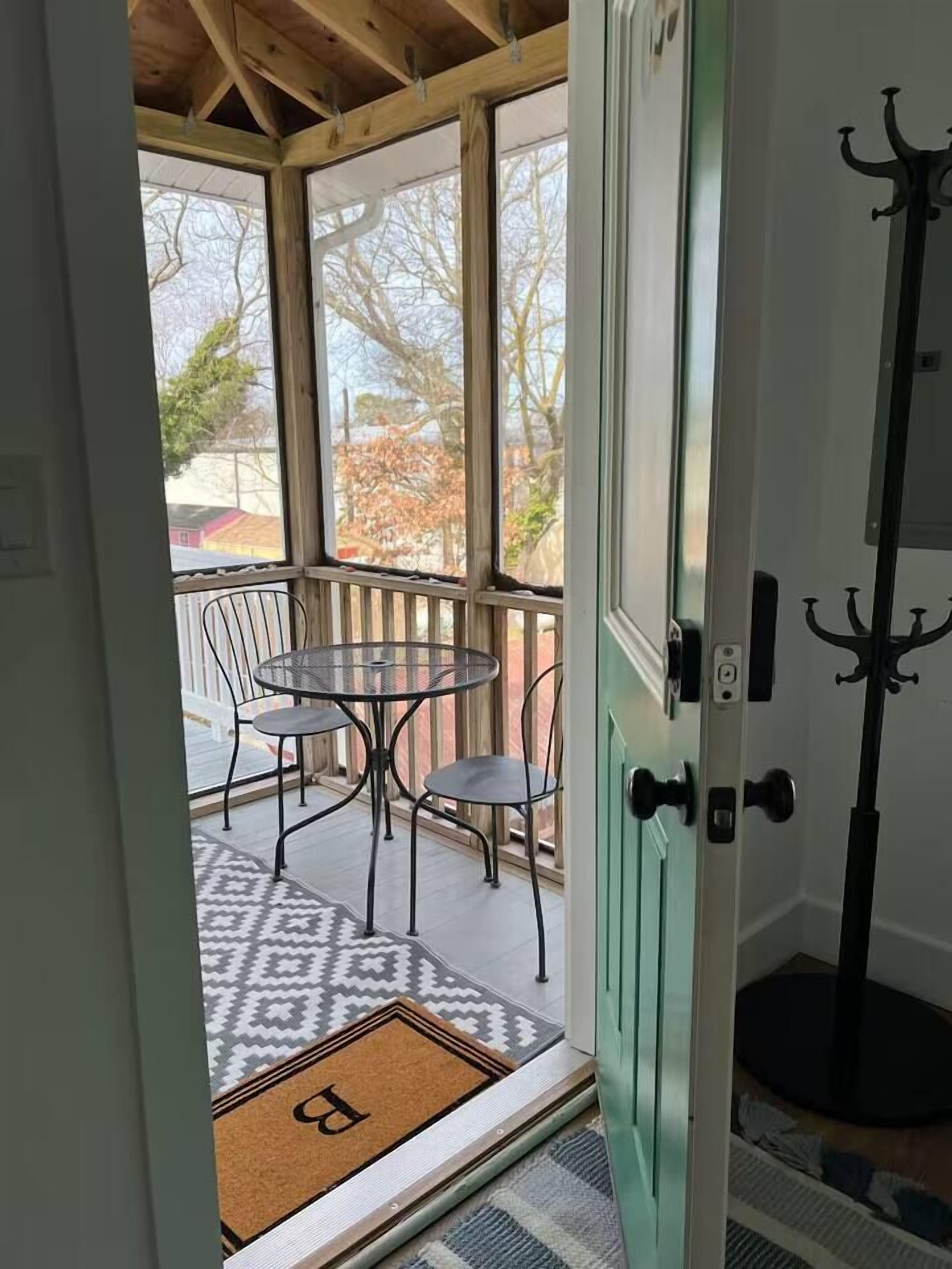 Eine überdachte Veranda mit Tisch, Stühlen, Kleiderständer und einer Tür mit Haken.
