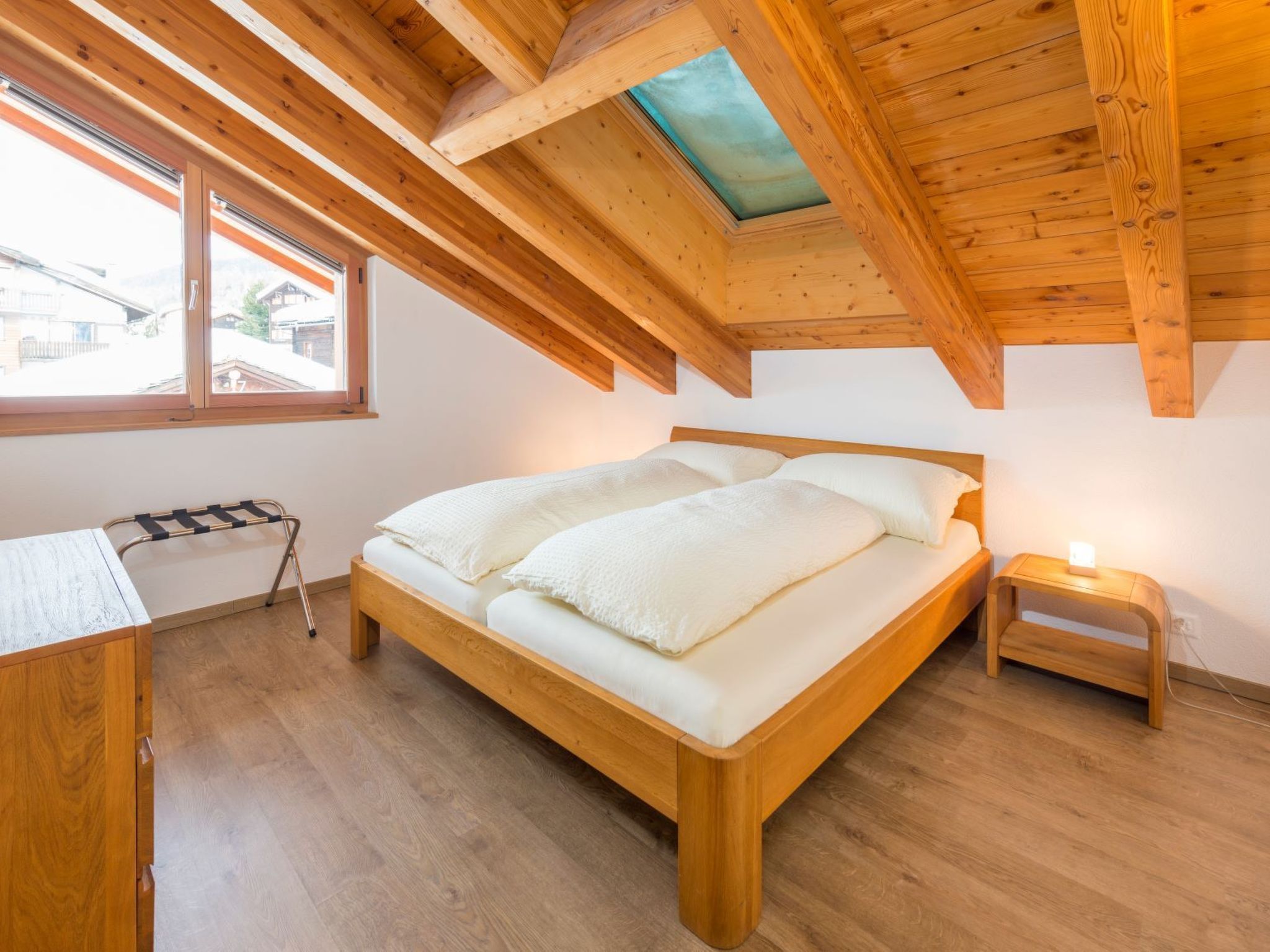Ein Schlafzimmer mit einem hölzernen Bett, einem kleinen Nachttisch, einem Fenster und einem Dachfenster.