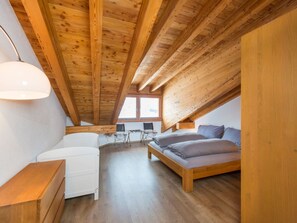 Un dormitorio acogedor en el ático, con techo de madera, cama, escritorio y silla.