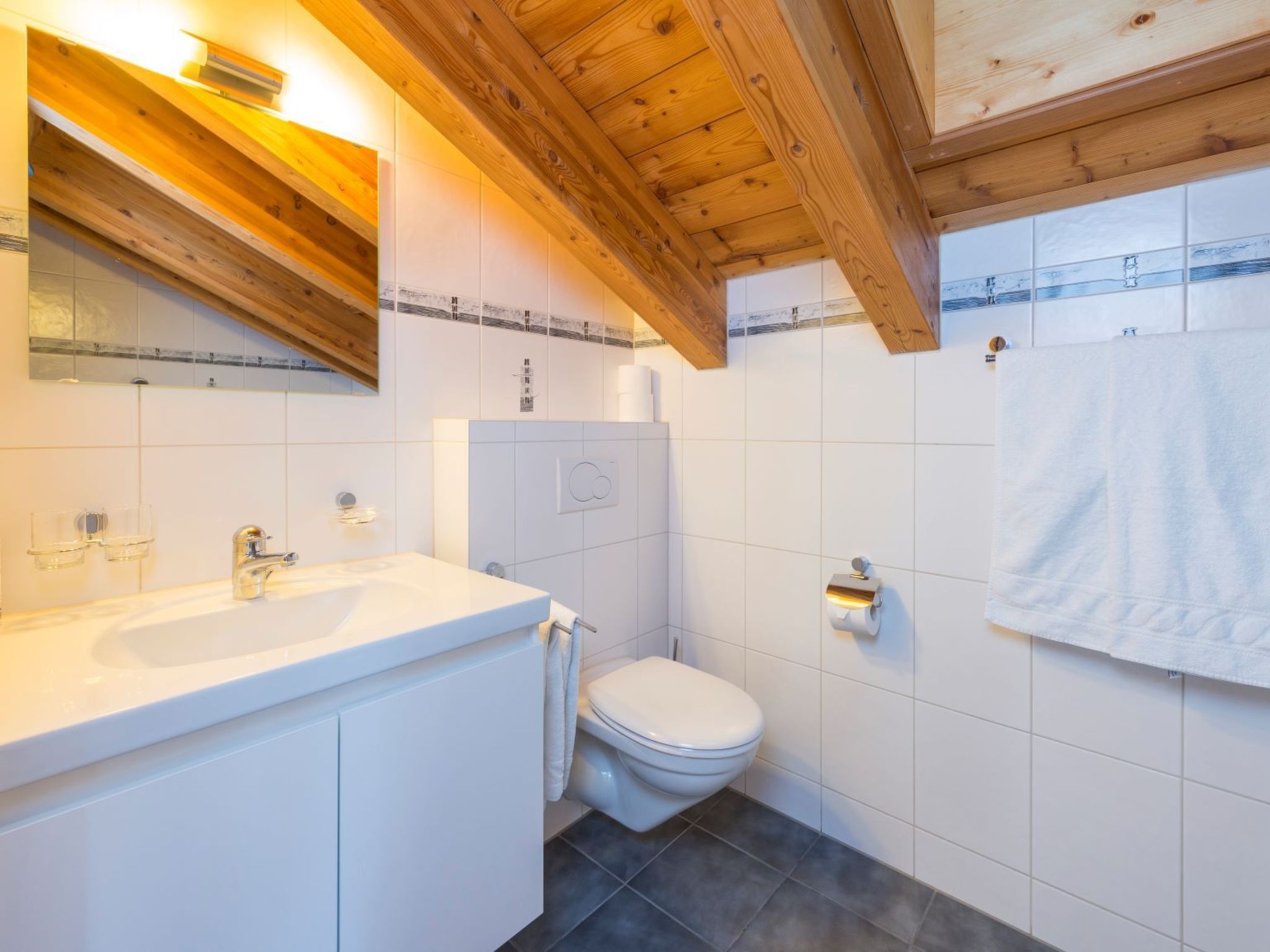 Ein Badezimmer mit Holzboden, weißen Fliesen, einem Waschbecken, einer Toilette und einem Handtuchhalter.