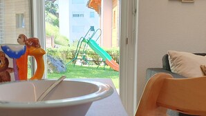 Ein Zimmer mit Fenster, einer Schale auf einem Tisch, einem Stuhl und Blick auf einen Spielplatz.