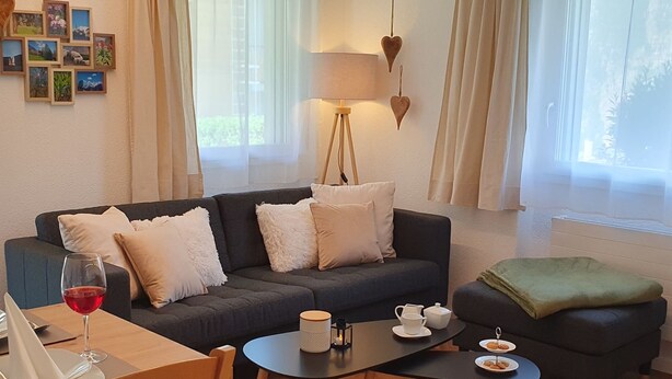 Ein gemütliches Wohnzimmer mit einer Couch, einem Couchtisch, einem Esstisch mit einem Weinglas und einer Lampe.