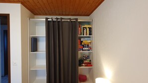 Ein Zimmer mit Holzboden, einem Bücherregal mit Büchern und Gesellschaftsspielen, einem Vorhang und einer Lampe.
