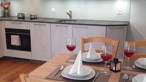 Eine moderne Küche mit Esstisch für zwei Personen, komplett mit weißem Serviettenkegel, Weingläsern und einer kleinen Vase mit Blumen.