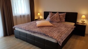 Ein Schlafzimmer mit einem großen Bett, zwei Nachttischen mit Lampen, einem Fenster mit Vorhängen und einem Holzboden.
