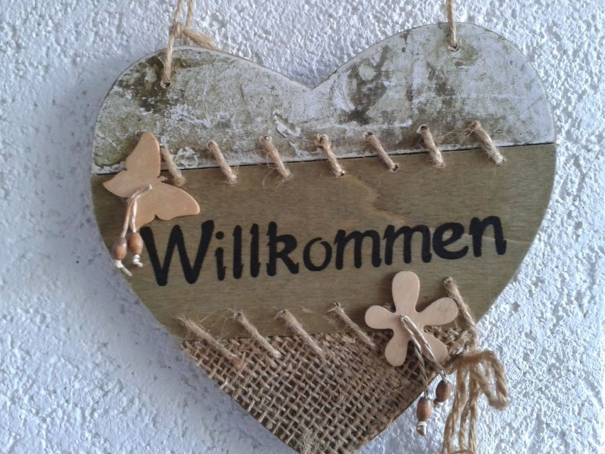 Ein herzförmiges Willkommensschild mit dem Wort 'Willkommen' und dekorativen Elementen.