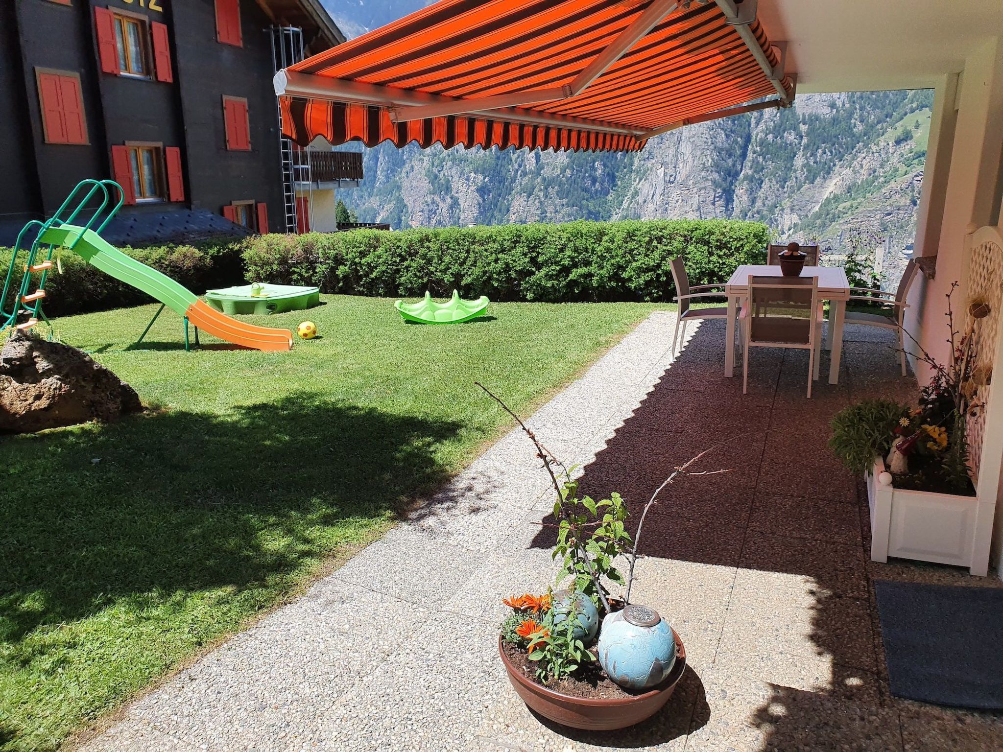 A patio area with a children's playset, a table with chairs, and a view of a mountainous landscape.