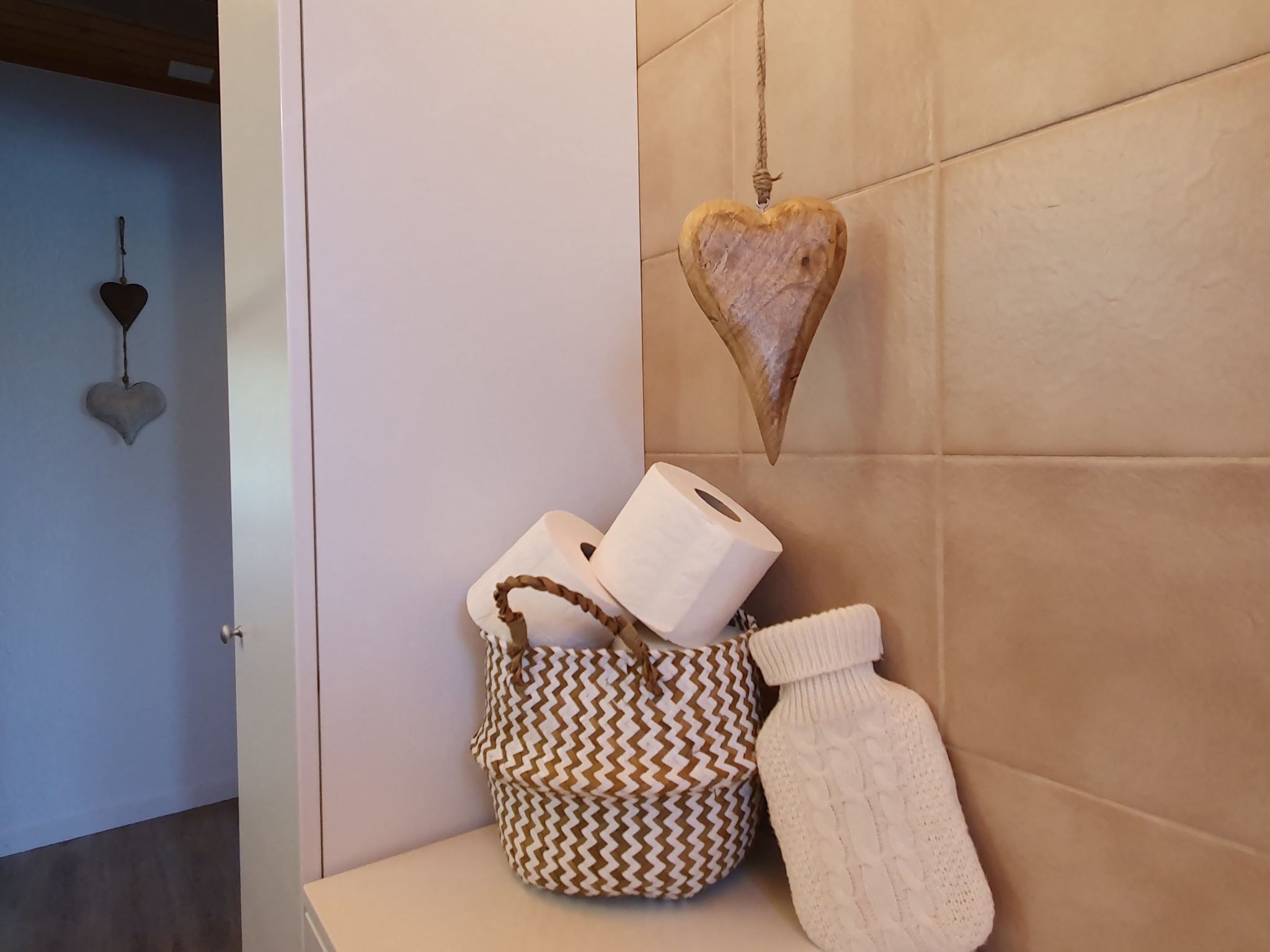 A bathroom with a white towel rack, a heart-shaped decoration, a patterned bag, and a white bathrobe.