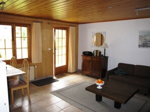 A living room with a wooden ceiling, a sofa, a coffee table, a dining area with a table and chairs, and a door with curtains. - Chalet Virginia A/B, (Grächen), by Interhome (Grächen)