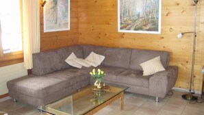 Una sala de estar con un sofá modular, una mesa de centro de vidrio y dos cuadros enmarcados en la pared.