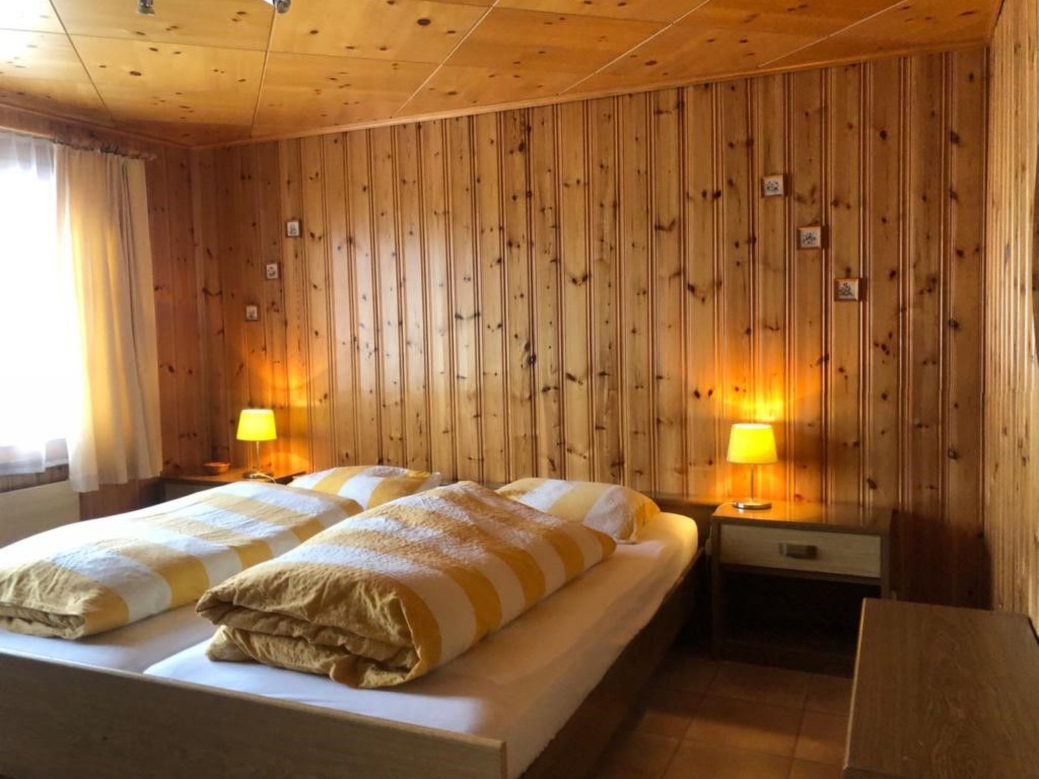 Ein Doppelzimmer mit zwei Betten, Holzwandverkleidung und Nachttischlampen.