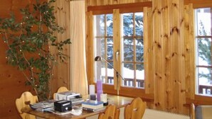 Interior de una cabaña de madera con una mesa de comedor, sillas, una lámpara roja, una ventana y una planta.