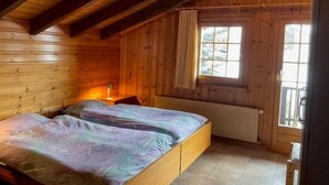 Un dormitorio de cabaña de madera con una cama, una ventana con cortinas y un radiador.
