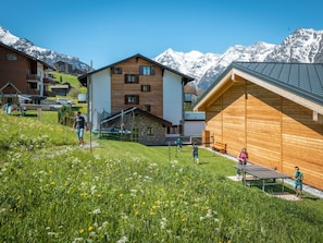 A residential area with wooden houses, a playground, and a mountain backdrop. - Ferienwohnungen Lunic, AZapartments.ch, B&B, (Grächen), 1057 by Interhome (Grächen)