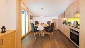 A compact kitchen with wooden cabinets, a dining table with chairs, and a small island with a kettle. - Lunic, AZapartments.ch, B&B, (Grächen), 1057 by Interhome (Grächen)