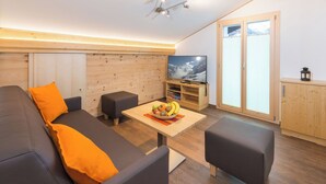 A modern living room with a sofa, ottoman, and a table with fruit. - Lunic, AZapartments.ch, B&B, (Grächen), 1057 by Interhome (Grächen)