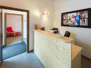 A reception area with a wooden desk, a red chair, a glass jar of candies, and a framed photo collage on the wall. - Ferienwohnungen Lunic, AZapartments.ch, B&B, (Grächen), 1057 by Interhome (Grächen)
