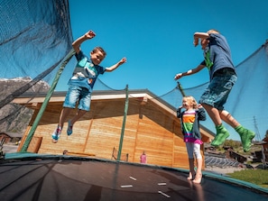 A trampoline with netted safety barriers, wooden flooring, and a clear blue sky in the background. - Ferienwohnungen Lunic, AZapartments.ch, B&B, (Grächen), 1057 by Interhome (Grächen)