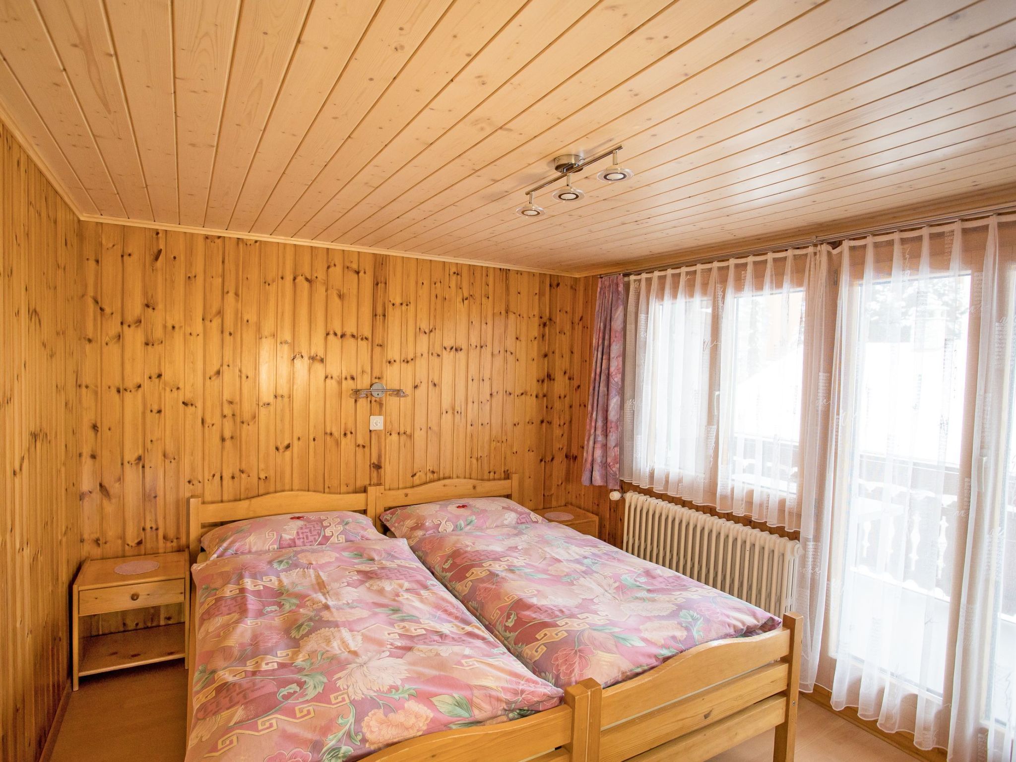 A wooden-paneled room with a bed, a nightstand, and a window with curtains.
