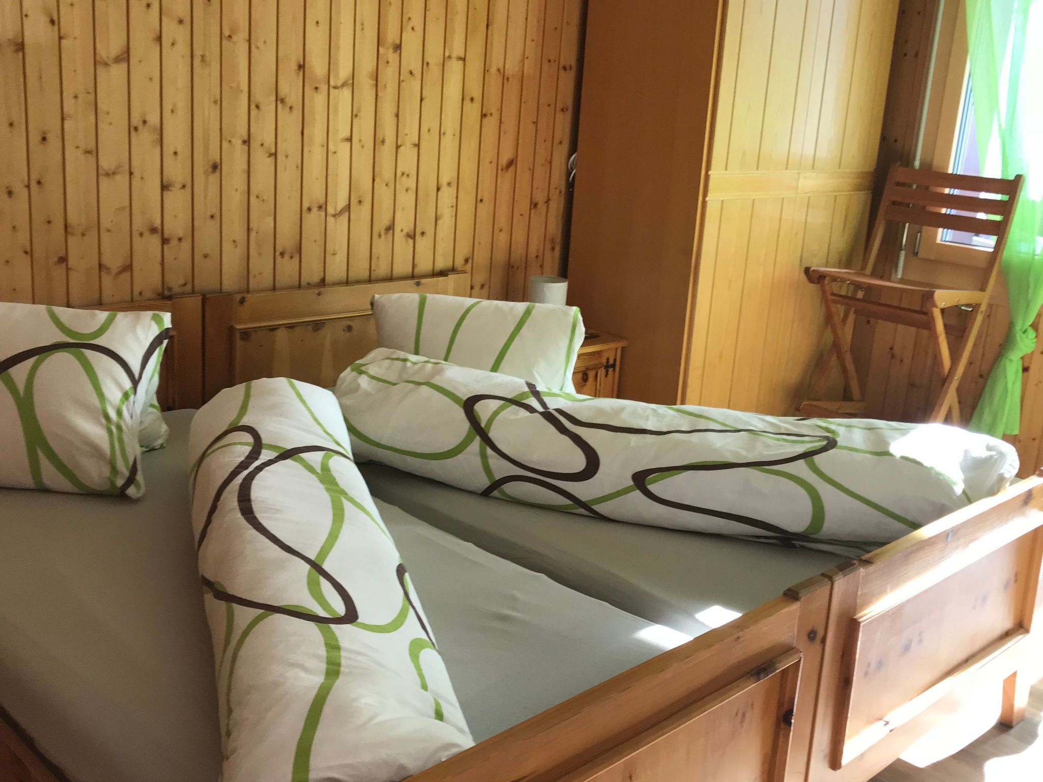 A wooden cabin room with a bed, pillows, and a chair.