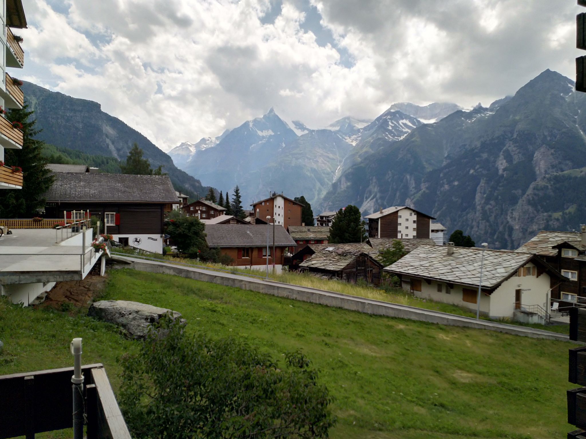 A mountain village with traditional buildings, a road, and snow-capped mountains in the background.