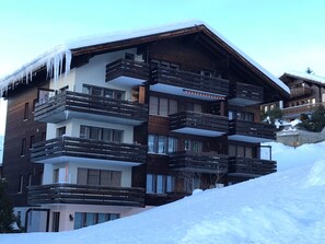 A multi-story hotel with balconies, wooden exterior, and snow on the roof. - Nr. 25 - Haus Opal, (Grächen), 1479 by Interhome (Grächen)